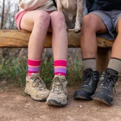 Colorful striped and neutral socks to wear with hiking boots, worn by two people sitting on a wooden bench with hiking boots on.