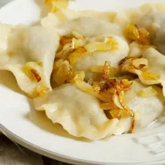 Pyszne pierogi ruskie na talerzu, polane skwarkami z cebulki. Idealne, gdy wiesz, jak długo gotować pierogi ruskie.