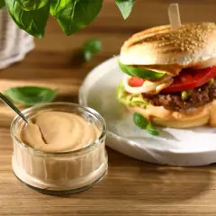 Burger z sosem w słoiczku i na talerzu, udekorowany bazylią.