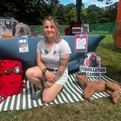 Une femme présente un stand sur la fibrillation canine, avec un mannequin de chien et du matériel de premiers secours. Elle enseigne le massage cardiaque chien.