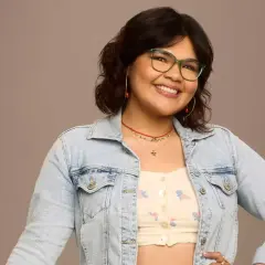 Belissa Escobedo, souriante, porte une veste en jean et des lunettes vertes. Elle est connue pour ses rôles dans des films et séries TV.