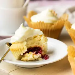 En närbild på en cupcake med vit frosting och en härlig röd fyllning. Flera liknande cupcakes med fyllning syns i bakgrunden.