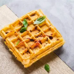 Goldbraune belgische Waffeln mit dunklem Sirup und frischem Basilikum, serviert auf einem Holzbrett.