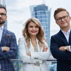 Trzy osoby w eleganckich strojach biznesowych stoją na tle nowoczesnych budynków.