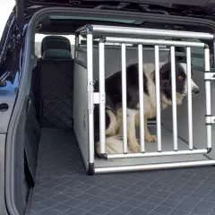 Un chien border collie dans une cage de transport en aluminium dans le coffre d'une voiture. La cage est bien positionnée, prête pour le voyage.