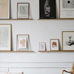 Bilderleiste dekorieren wohnzimmer: Mehrere gerahmte Kunstwerke und Karten zieren zwei schlichte Holzregale, die eine stilvolle Wandgestaltung im Wohnzimmer bilden.