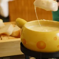 Un pezzo di pane viene intinto in una fonduta di formaggio filante, un modo delizioso per fondere il formaggio.