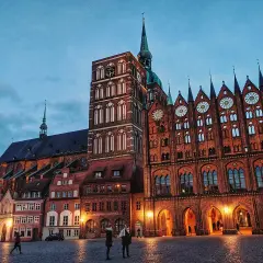 Abendstimmung im **Stralsund Zentrum**: imposante Backsteingotik mit Kirchturm und Rathaus, beleuchteter Marktplatz mit wenigen Passanten.