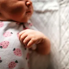 Małe niemowlę zaciska piąstki i się napina, ubrany w pajacyk w truskawki.