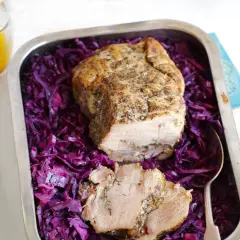 Soczysta łopatka pieczona z ziołami, podana na purpurowej kapuście w metalowej tacce. Obok dzbanuszek z żółtym sosem.