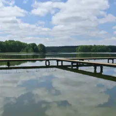 Spokojne jezioro na Mazurach z drewnianymi pomostami. Trudno policzyć, ile jest jezior na Mazurach, ale to jedno z nich zachwyca odbiciem chmur.