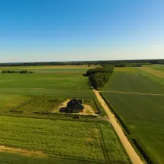 Dom w budowie na tle pól i lasu, co wymaga pozwolenia na budowę. W oddali widać farmę wiatrową.