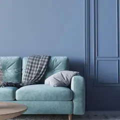 Miętowa kanapa z kocem i poduszką na tle ścian w kolorze baby blue. To znaczy spokój i świeżość.