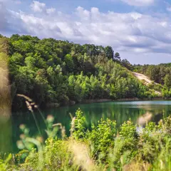Turkusowe jezioro Wapnica otoczone bujną zielenią, z piaszczystym zboczem w tle.
