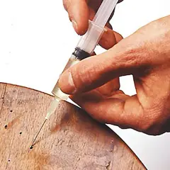 Mano inietta liquido da siringa in fori su legno, per eliminare tarli legno alcool.
