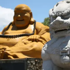 Złoty Budda i kamienna lwica strażniczka na tle błękitnego nieba.