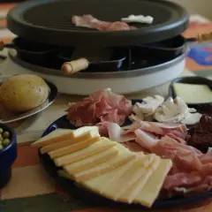 Préparation d'une raclette conviviale : fromage, charcuterie, pommes de terre et petits pois attendent sur la table.