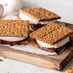Drei S'mores Cookies mit geschmolzener Schokolade und Marshmallows auf einem Holzbrett.