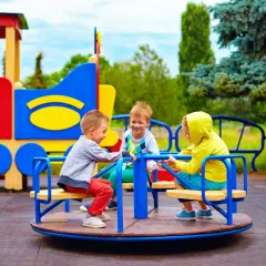 Trzech chłopców śmieje się na karuzeli, czekając, kiedy zostaną otwarte place zabaw dla dzieci.