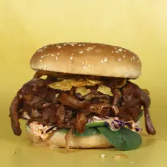 Hamburguesa con pulled pork vegano, cebolla caramelizada y crujientes patatas fritas sobre fondo amarillo.