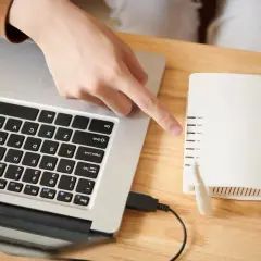 Ręka wskazuje na router, podłączony do laptopa. Dowiedz się, jak połączyć się z drukarką HP.