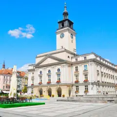 Rynek w mieście nad Prosną. Ratusz z wieżą zegarową góruje nad placem, gdzie stoją stoliki kawiarniane.