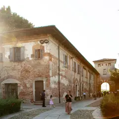 Passeggiata serale all'abbazia di Chiaravalle, con edifici storici in mattoni e un arco d'ingresso illuminato dal sole.