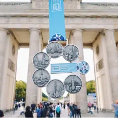 Medal za ukończenie korony maratonów świata przed Bramą Brandenburską. Widoczne miasta: Boston, Tokio, Nowy Jork, Chicago, Berlin, Londyn.