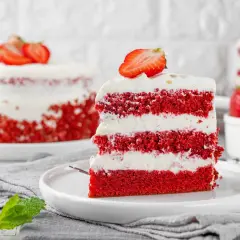 Kawałek tortu red velvet z kremem i truskawkami na talerzu.
