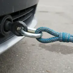 Dłoń trzymająca linę holowniczą zaczepioną do haka holowniczego samochodu.