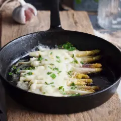 Szparagi zapiekane z serem, podane w żeliwnej patelni, posypane natką pietruszki.