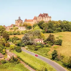Un village pittoresque en France, idéal pour savoir où partir en France en mai. Un château domine la colline verdoyante.