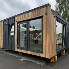 Nowoczesne domy modułowe pod klucz, z drewnianą i grafitową elewacją, dużymi oknami i drzwiami tarasowymi.