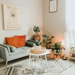 Gemütliches kleines Wohnzimmer skandinavisch einrichten mit grauem Sofa, orangefarbenen Kissen, Pflanzen und einem inspirierenden Bild.