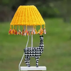 Lámpara techo infantil con pantalla tejida amarilla y borlas de colores. La base es una figura de llama blanca y negra.