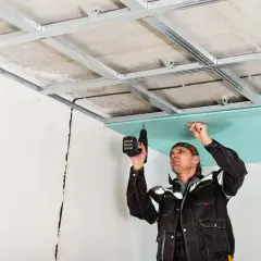 Un ouvrier réalise la pose de suspente et fourrure pour un faux plafond en plaques de plâtre bleu.