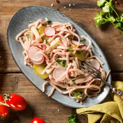 Ein köstlicher low carb picknick Teller mit Wurstsalat, Radieschen, Gewürzgurken und Tomaten auf rustikalem Holztisch.