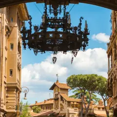 Un imponente lampadario domina la vista del quartiere Coppedè, incorniciato da palazzi storici e un cielo azzurro con nuvole bianche.