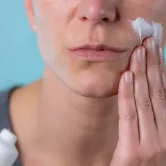 Kobieta aplikuje na twarz kremową bazę 10. Delikatna pielęgnacja dla promiennej cery.