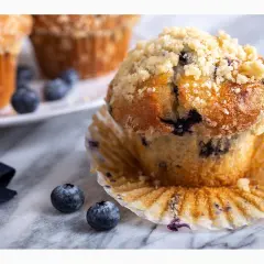 Saftige Blaubeermuffins mit Streuseln, perfekt für ein Blaubeermuffins Rezept. Frische Blaubeeren liegen daneben.