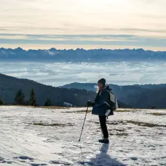 Kobieta z kijkami trekkingowymi na ośnieżonym szczycie, podziwiająca Tatry. To najładniejsza trasa na Turbacz zimą.