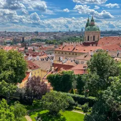 Widok na dachy Pragi z zielonym ogrodem. W oddali widać kopułę kościoła. Idealne miejsce, by zobaczyć w Pradze piękno architektury.