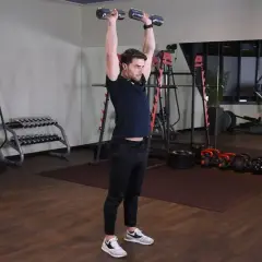 Wyciskanie hantli nad głowę angażuje mięśnie naramienne i triceps. Mężczyzna wykonuje ćwiczenie w siłowni.