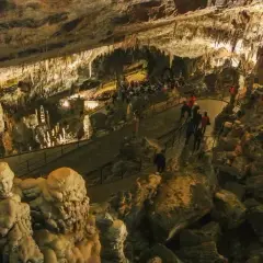 Wspaniałe formacje skalne w jaskini Postojna, gdzie turyści spacerują po oświetlonych ścieżkach wśród stalaktytów i stalagmitów.