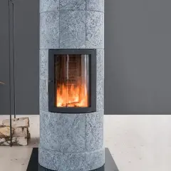 Poêle en pierre ollaire aux flammes vives, avec une décoration de faisan et de bois de chauffage à proximité.