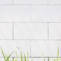 Biała ściana z bloczków silikatowych, z zieloną trawą u dołu.