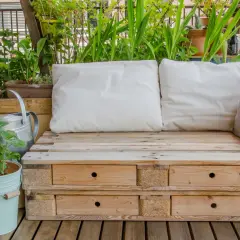 Bequeme Sitzbank aus Paletten mit Schubladen, umgeben von grünen Pflanzen. Tolle Ideen aus Paletten für Balkon und Garten.