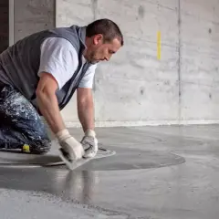 Man knäböjer och drar en spackel över golvet för att jämna ut flytspackel som ytskikt.