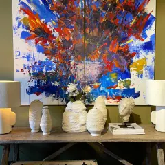 Lámpara de mesa infantil con diseño moderno, junto a jarrones texturizados y un cuadro abstracto vibrante.