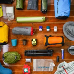 A collection of gear for a backpacking trip: dry bags, sleeping pad, socks, hat, first aid kit, water bladder, and more.